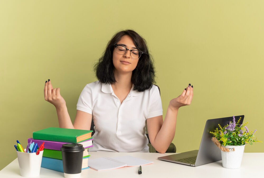 young-pleased-pretty-caucasian-schoolgirl-wearing-glasses-sits-desk-with-school-tools-pretends-meditate-with-raised-hands-isolated-green-space-with-copy-space